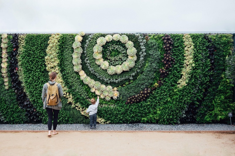 mother and child standing in front of a mural made of plants