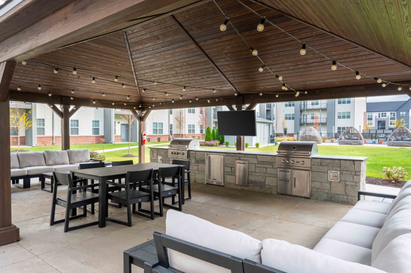 a covered outdoor patio with seating tables grills and a tv